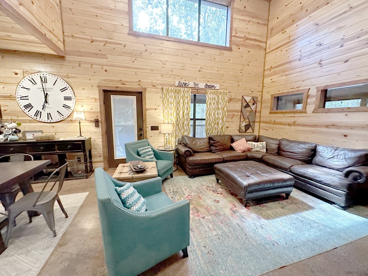 Great room at Livin' the Dream with a brown leather sectional, two teal armchairs, a large wall clock and pine plank walls