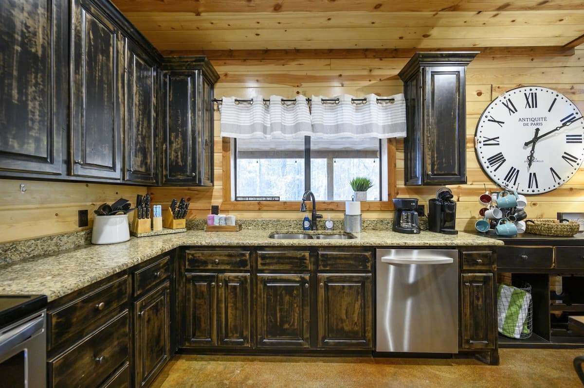Kitchen at Livin' the Dream with dark distressed cabinets, granite counters, a stainless dishwasher and a window over the sink
