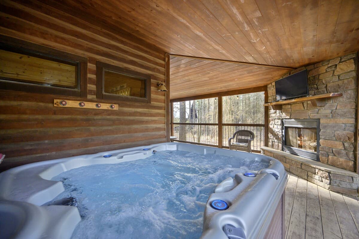 Hot tub on the covered back deck at Livin' the Dream, beside a stone gas fireplace with a TV above it