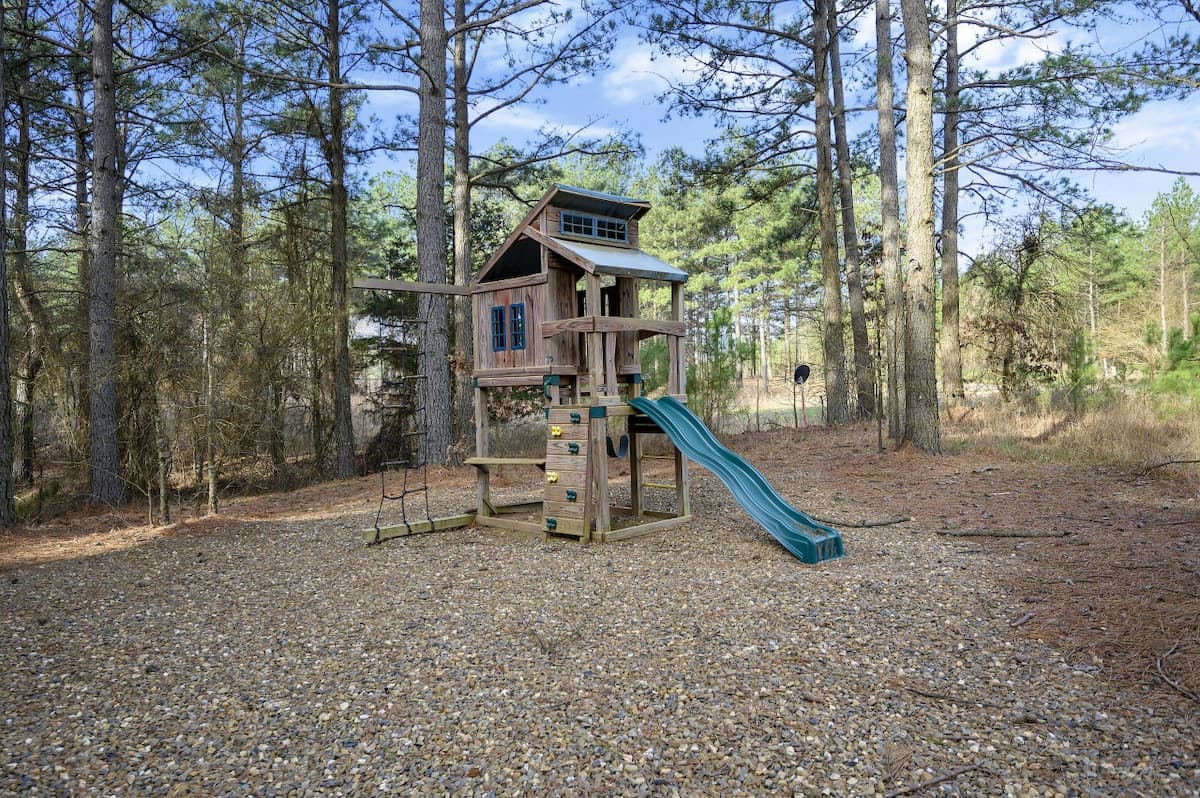 Wooden playset with a fort, swings and a green slide among the pines at Livin' the Dream