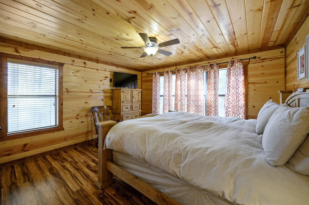 Second upstairs bedroom at Livin' the Dream with a pine bed, a wall of windows with patterned curtains and a ceiling fan