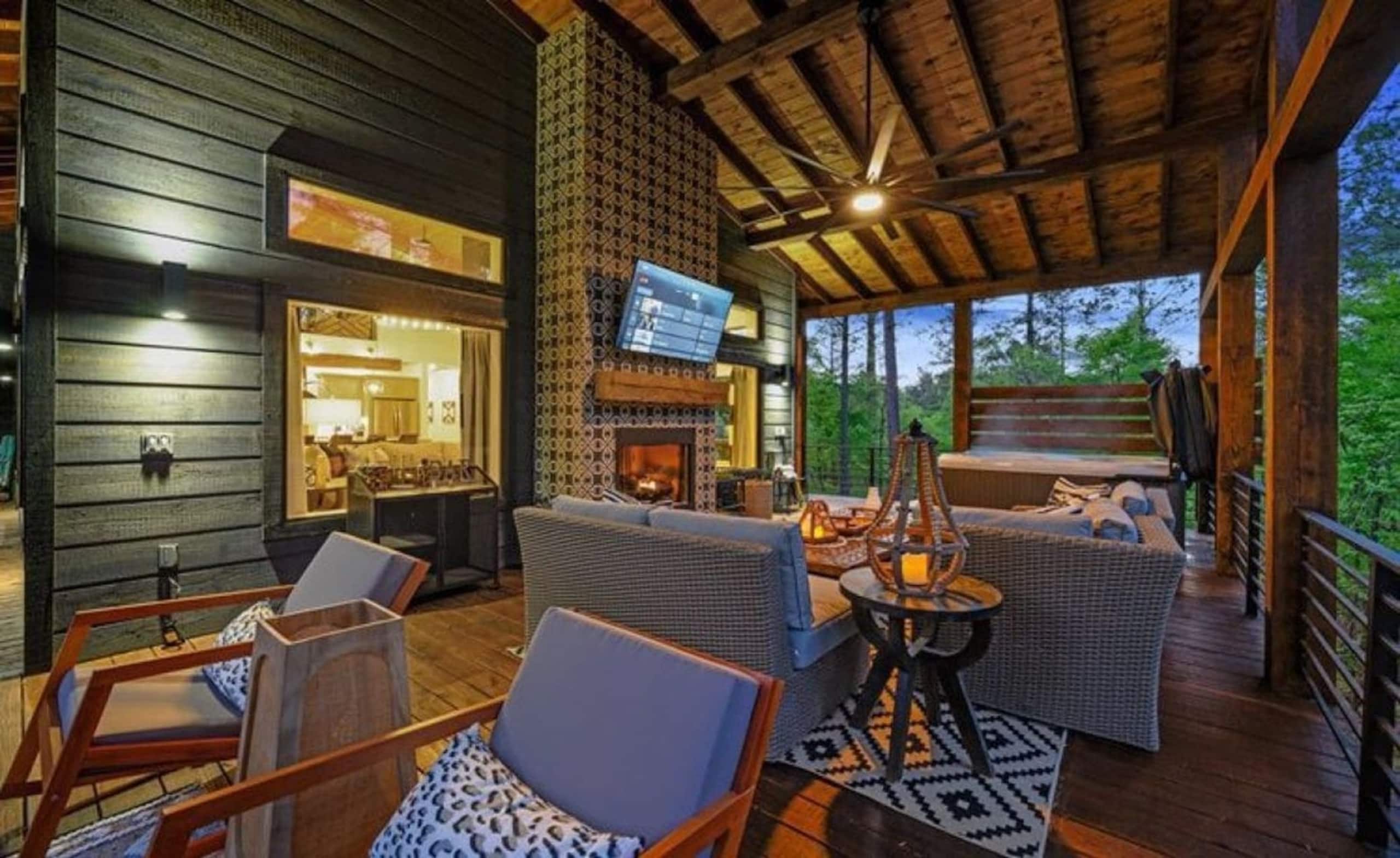 Covered deck at Sublime Retreat with lounge chairs around an outdoor fireplace and TV, the hot tub behind
