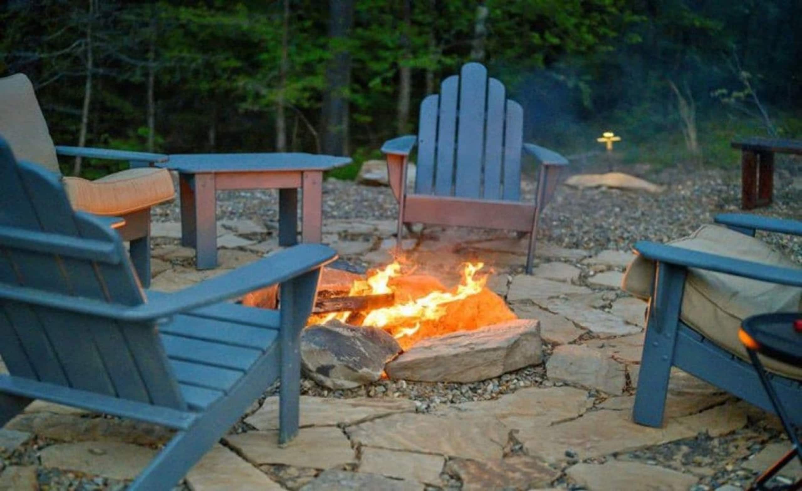 Fire pit at Sublime Retreat with a stone surround and blue Adirondack chairs