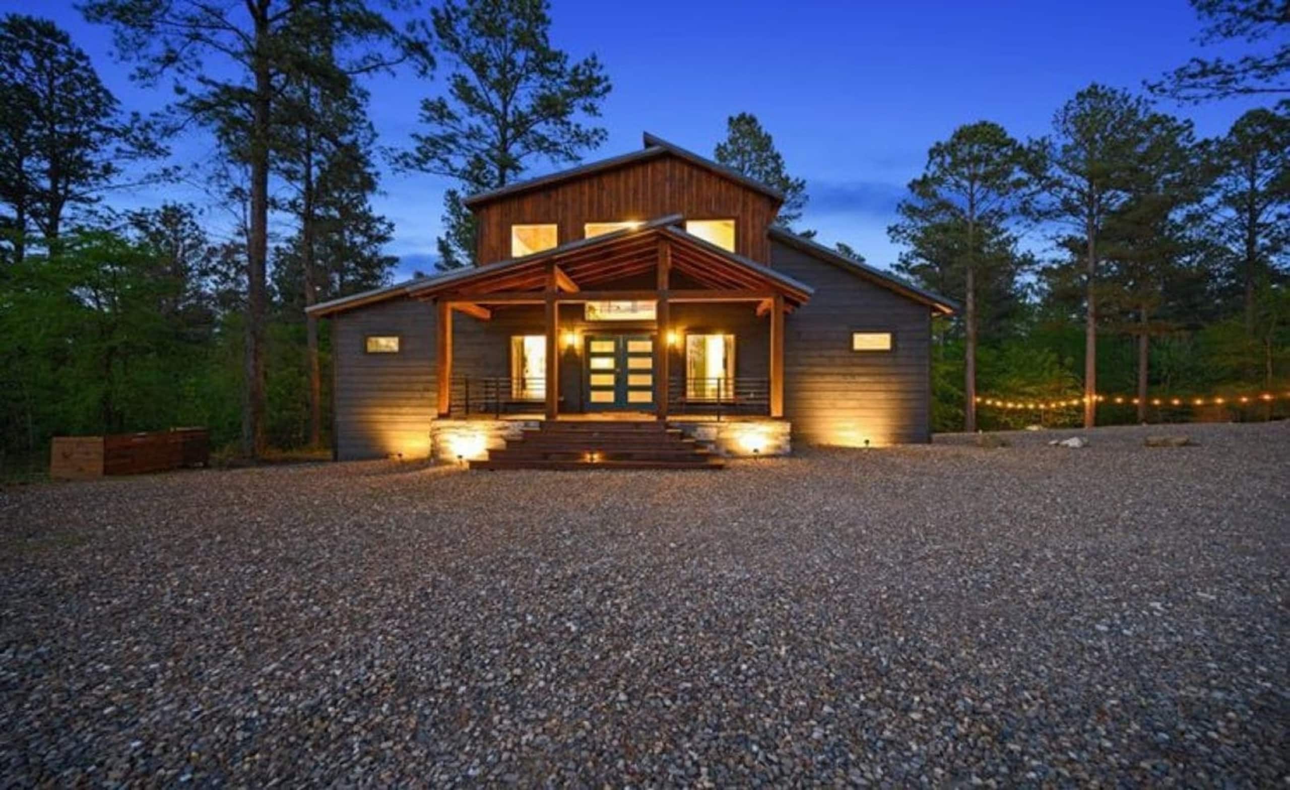 Front of Sublime Retreat at dusk, with a lit porch, a gravel drive and string lights in the pines