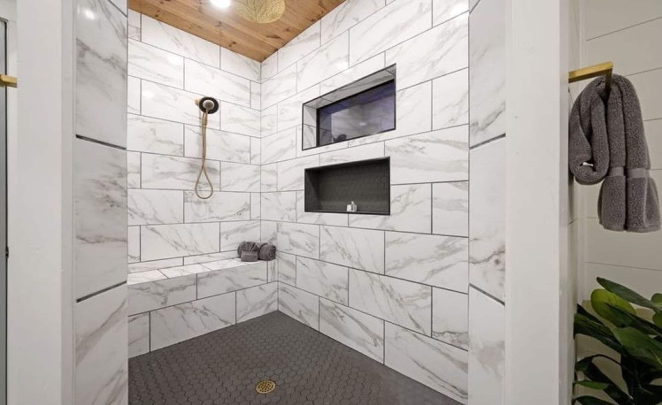 Walk-in shower at Sublime Retreat with marble-look tile, a built-in bench and a wood-plank ceiling